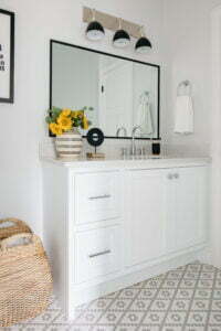 Custom made white bathroom vanity with silver hardware, a matte black mirror, flowers in a vase, a chrome faucet, and matte black pendant lighting.