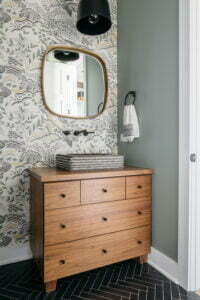 Stylish powder room with patterned wallpaper, a walnut vanity, a concrete sink sitting on the counter, and a rounded mirror.