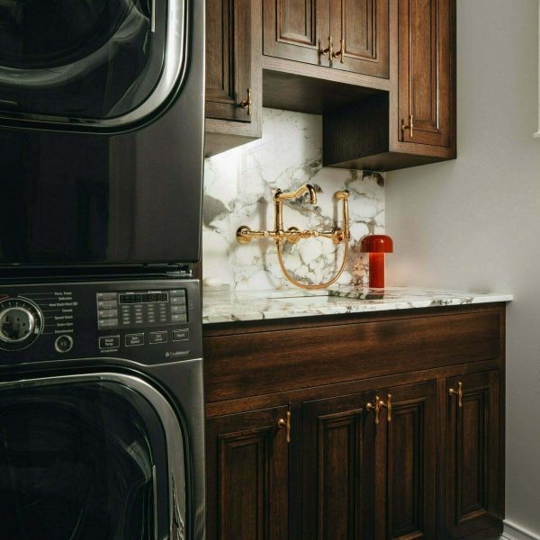 Luxury dark wood laundry room cabinets with a marble backsplash and black laundry machines.